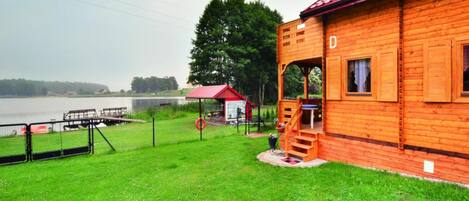 A wooden cabin with a red roof, a small porch, and a view of a lake.