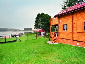 A wooden cabin with a red roof, a small porch, and a view of a lake. - Wooden House by Ostrowieckie Lake With Beach (Malechowo)