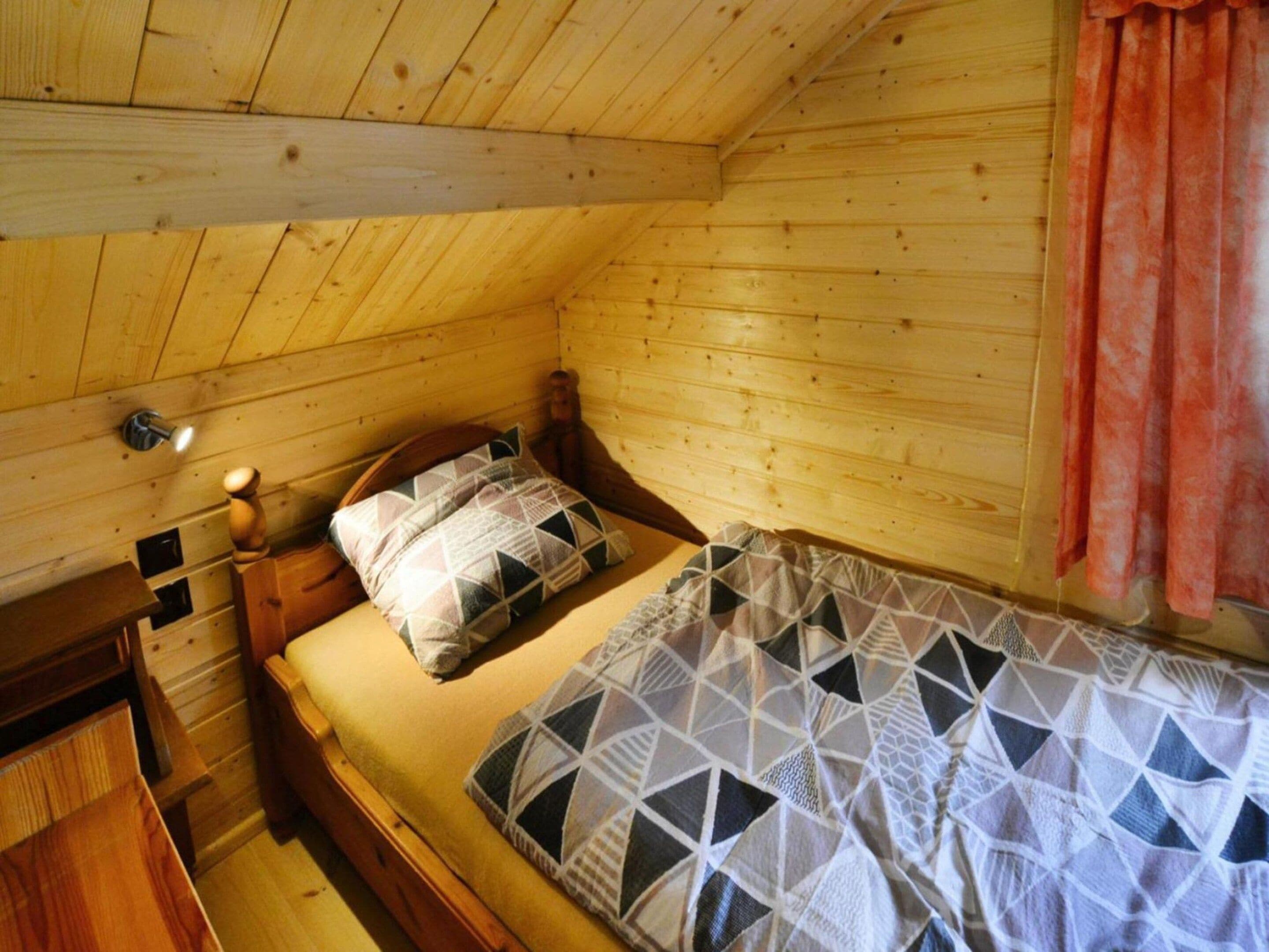 Une chambre dans une cabane en bois, avec un lit simple, une table de chevet, une lampe et une fenêtre avec des rideaux.