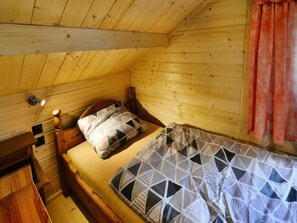 A wooden cabin bedroom with a single bed, a nightstand, a lamp, and a window with curtains. - Wooden House by Ostrowieckie Lake With Beach (Malechowo)