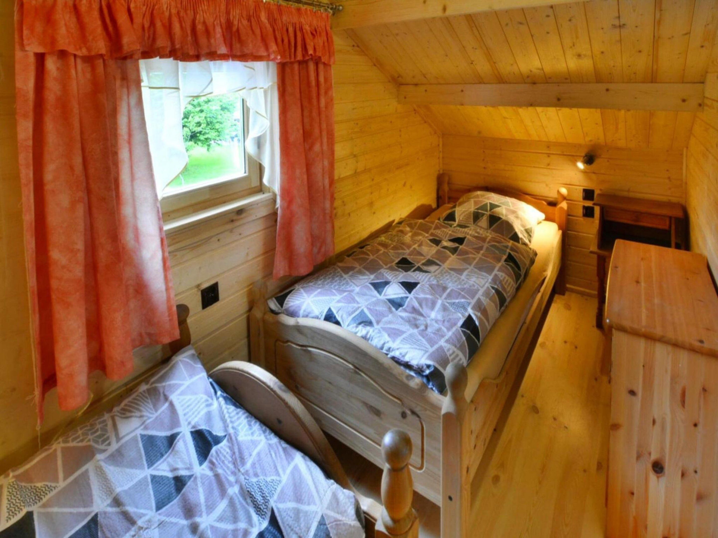 A single bed in a cabin with a window, wooden walls, and a small table.