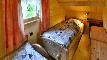 A single bed in a cabin with a window, wooden walls, and a small table.