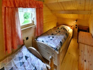 A single bed in a cabin with a window, wooden walls, and a small table. - Wooden House by Ostrowieckie Lake With Beach (Malechowo)