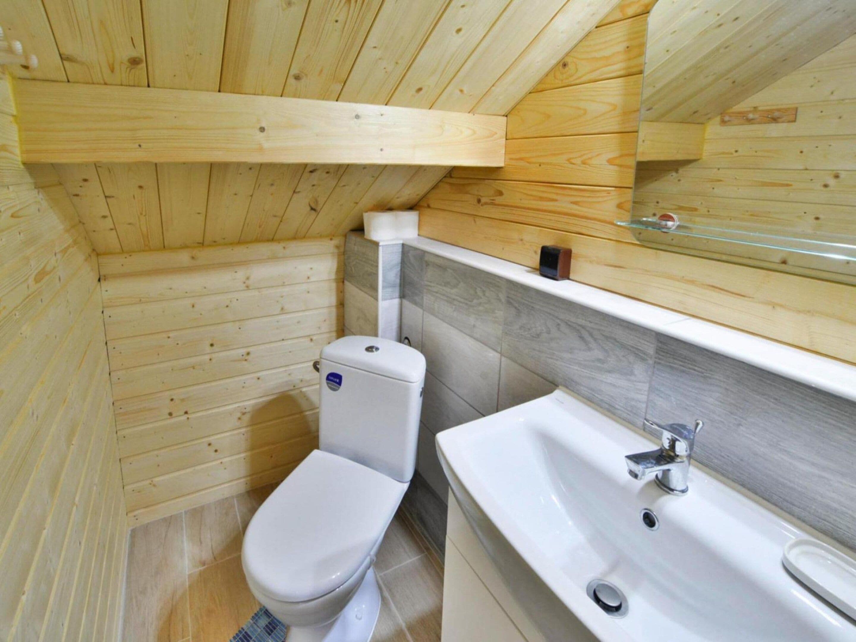 Een badkamer met houten lambrisering, een toilet, een wastafel en een spiegel.