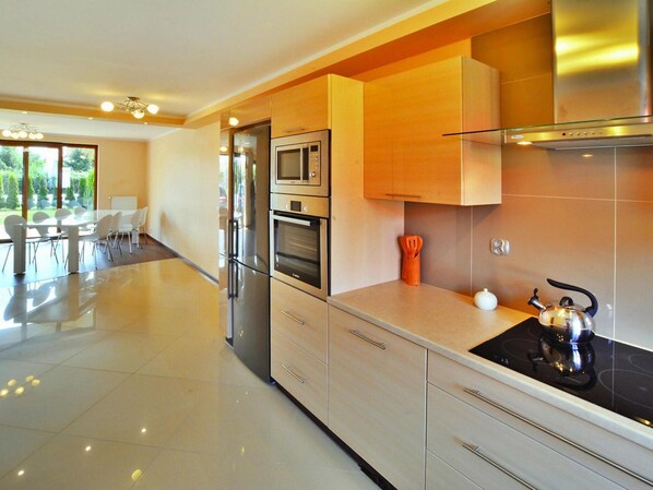A modern kitchen with stainless steel appliances, wooden cabinets, and a dining area with a glass table and chairs.