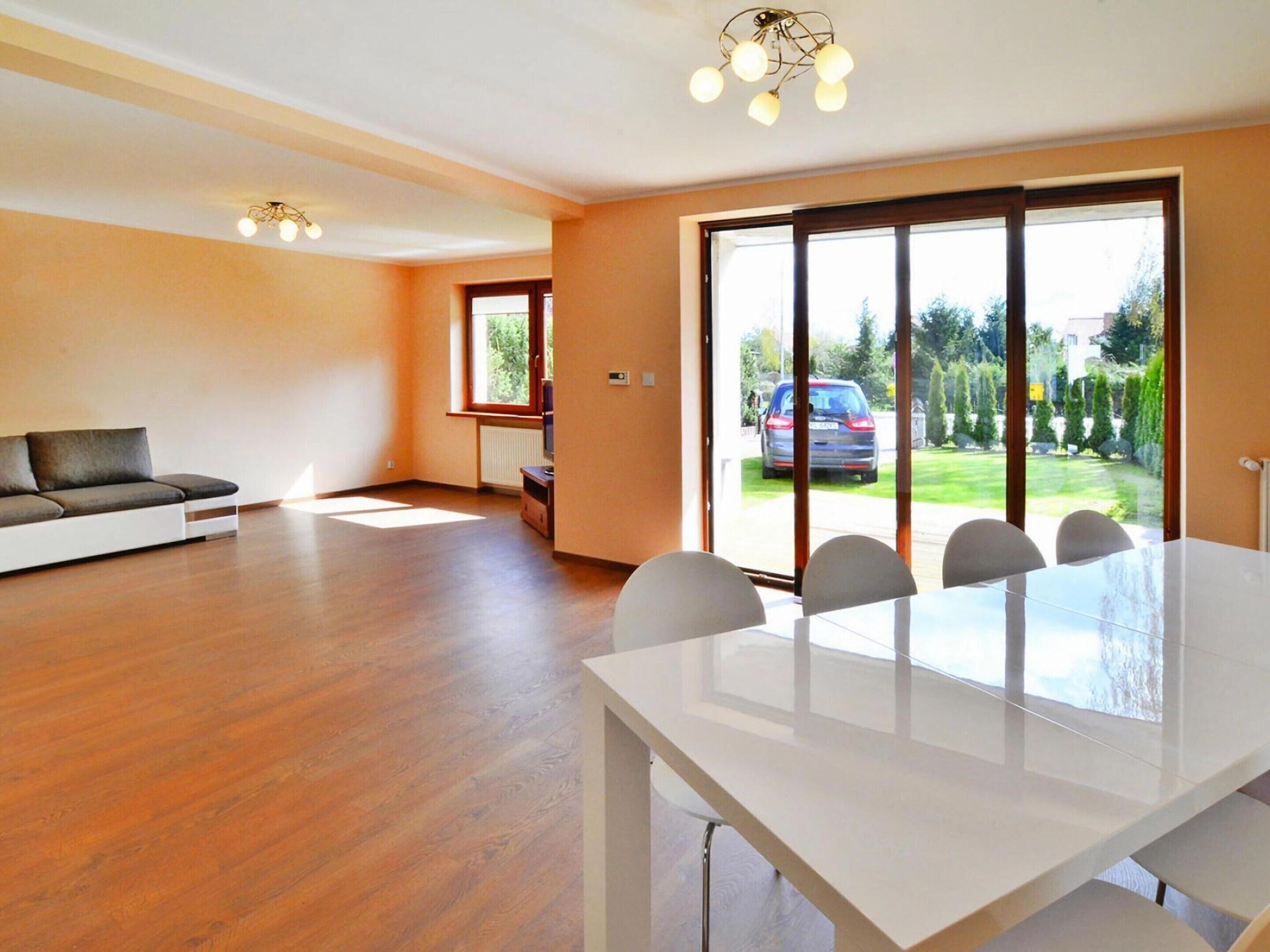 A spacious living room with a sofa, a dining table with chairs, a TV, and a sliding glass door leading to a garden.