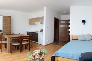 Ein modernes, kompaktes Zimmer mit einem Holztisch, einer Küchenzeile und einem Bett mit blauer Decke.