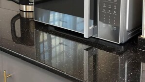 A modern kitchen with a stainless steel microwave, a coffee maker, and a kettle on the countertop. - LivLuxe Apartments 7 (Kampala)