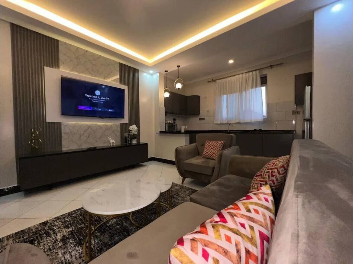 A modern living room with a flat-screen TV, a sofa, a coffee table, and a kitchen in the background.