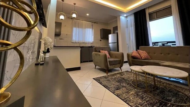 A modern living room with a sofa, coffee table, and a kitchen in the background. - LivLuxe Apartments 7 (Kampala)