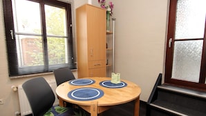 A dining area with a wooden table, two chairs, a cabinet, and a window with blinds.