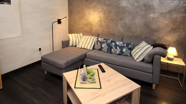 A modern living room with a grey sectional sofa, a small wooden coffee table, a floor lamp, and a wall-mounted shelf.