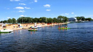 A calm lake with several small boats, a sandy beach, and a row of trees in the background. - Holiday Home in Stepnica Near Szczecin Lagoon (Stepnica)