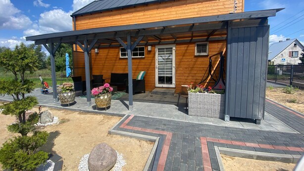 A modern wooden house with a covered patio, outdoor seating, and potted plants. - Holiday Home in Stepnica Near Szczecin Lagoon (Stepnica)