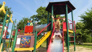 Une aire de jeux avec un toboggan rouge, des structures d’escalade et un espace de jeux abrité.
