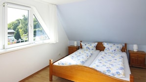 Une chambre à coucher avec un lit en bois, deux tables de chevet, une fenêtre avec des rideaux et une vue sur la verdure.