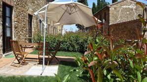 A patio with a table and chairs, a white umbrella, and a stone building in the background. - Apartment in Campiglia Marittima (Campiglia Marittima)