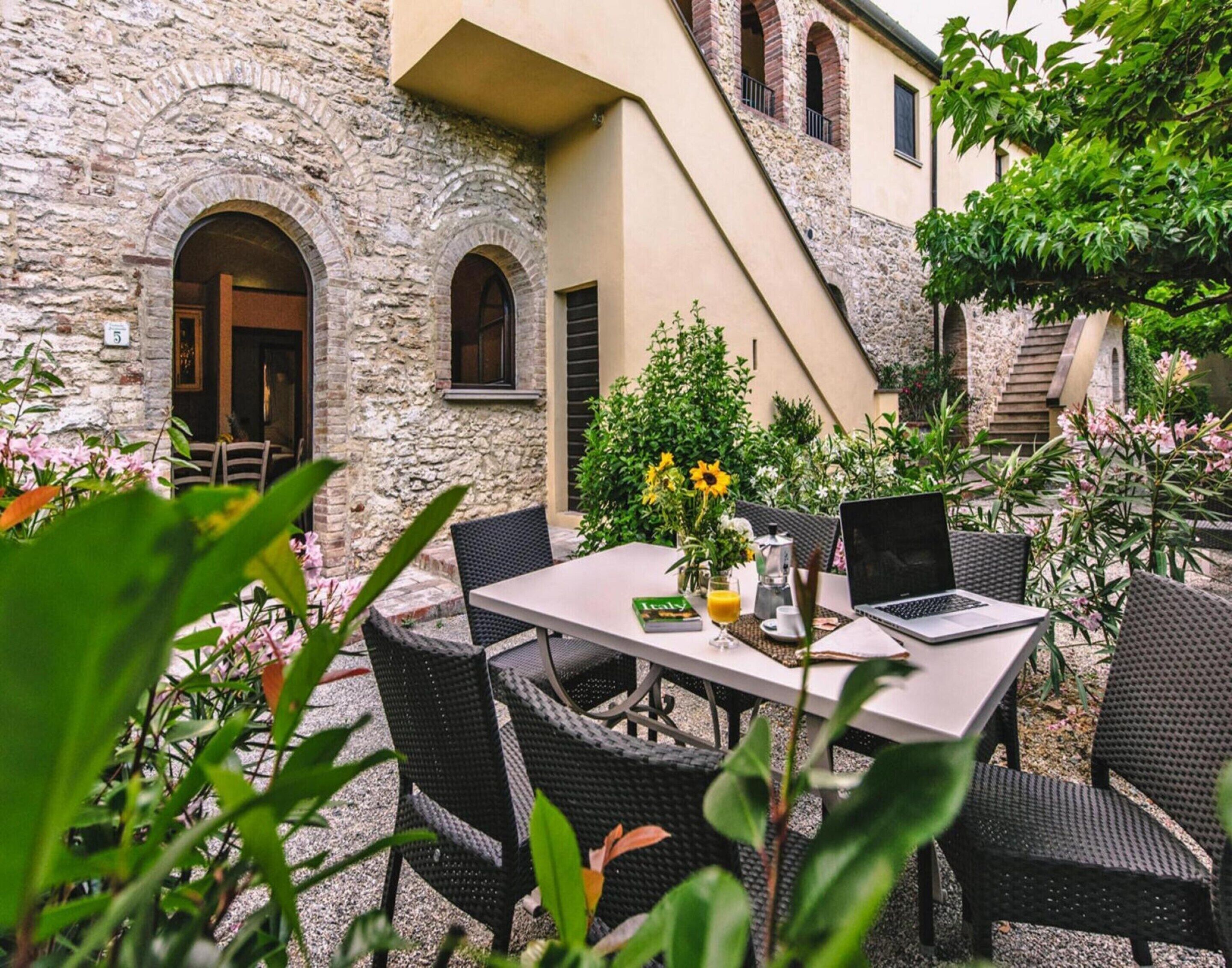 Un espacio de comedor al aire libre con un edificio de piedra, una mesa con sillas y una computadora portátil.