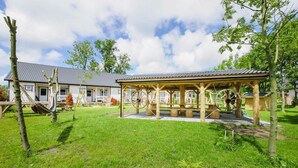 A wooden gazebo with a metal roof, surrounded by a grassy area and trees. - Apartment in a Family Holiday Resort (Postomino)