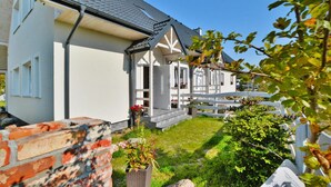 A two-story house with a white exterior, grey roof, and a small front porch with potted plants. - Apartment in a Family Holiday Resort (Postomino)