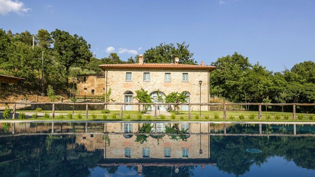 Un bâtiment en pierre avec une piscine devant, entouré d’arbres et de verdure.