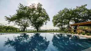 Une piscine aux eaux cristallines, entourée d’arbres, avec une pergola en bois d’un côté.