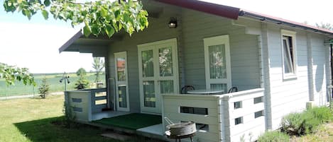 Una casa pequeña de un piso con porche, una mesa y una parrilla en el exterior.