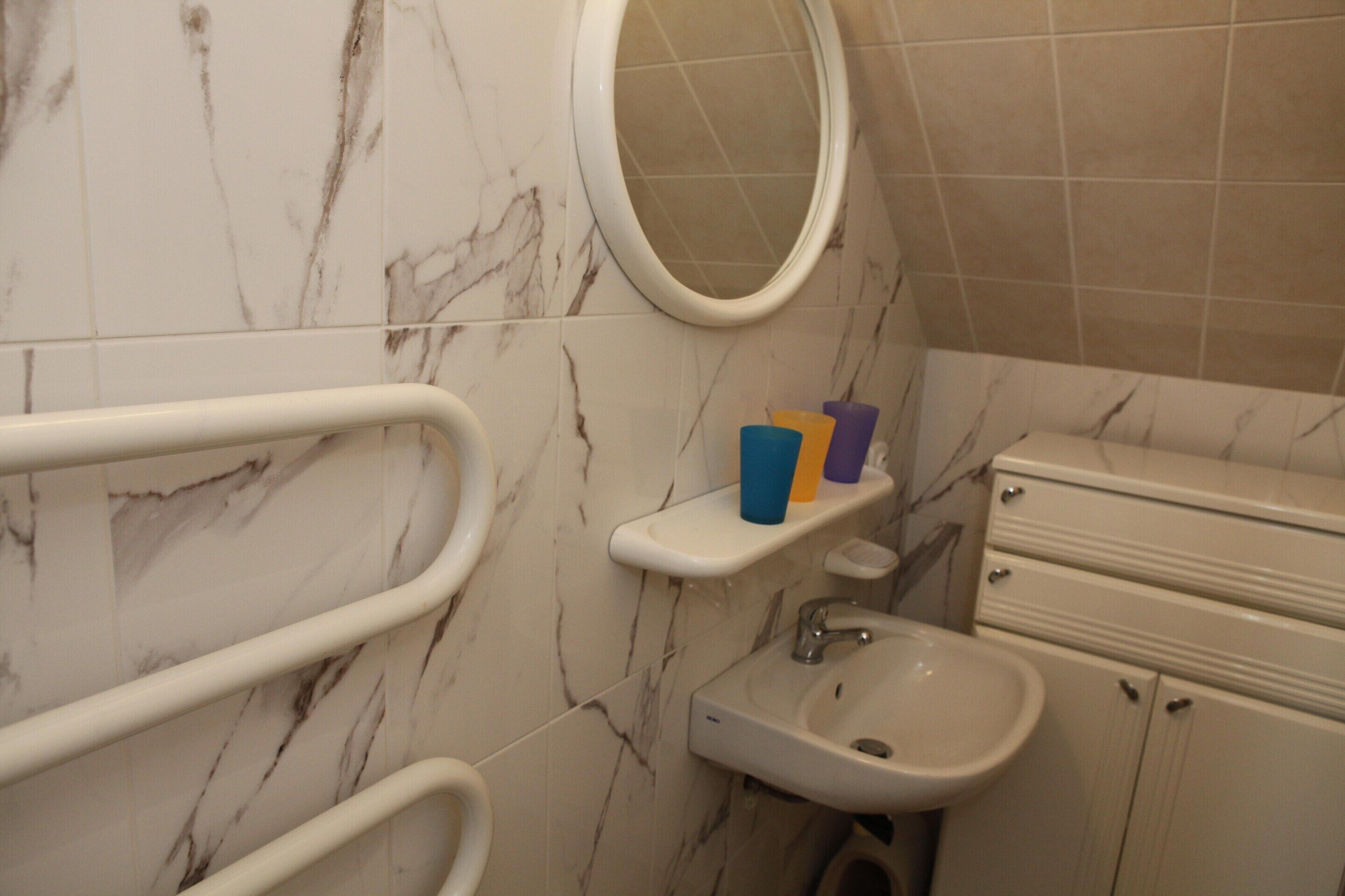 Un baño con pared de mármol, un espejo redondo, un lavabo, un inodoro y un armario de almacenamiento.