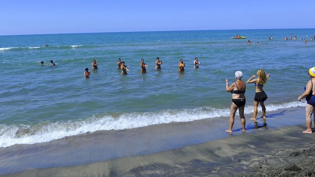 Una playa con gente nadando y de pie en el agua.