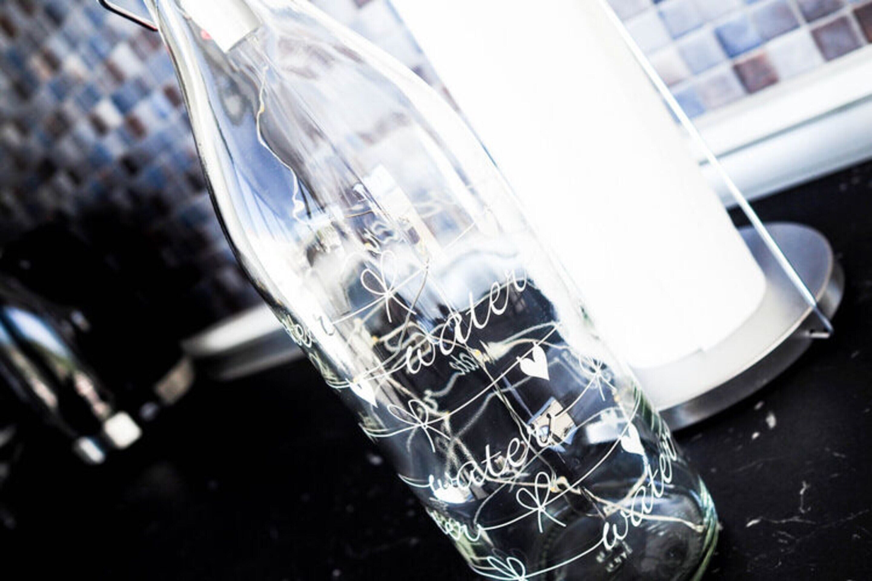 Une bouteille en verre transparent ornée de motifs gravés et d’un symbole en forme de cœur, posée sur une surface sombre.