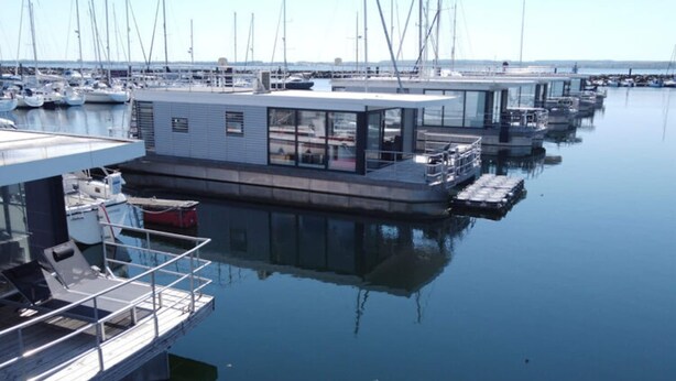 Ein Yachthafen mit mehreren vertäuten Booten und einer modernen schwimmenden Struktur mit Glasfassade und Sitzbereich.