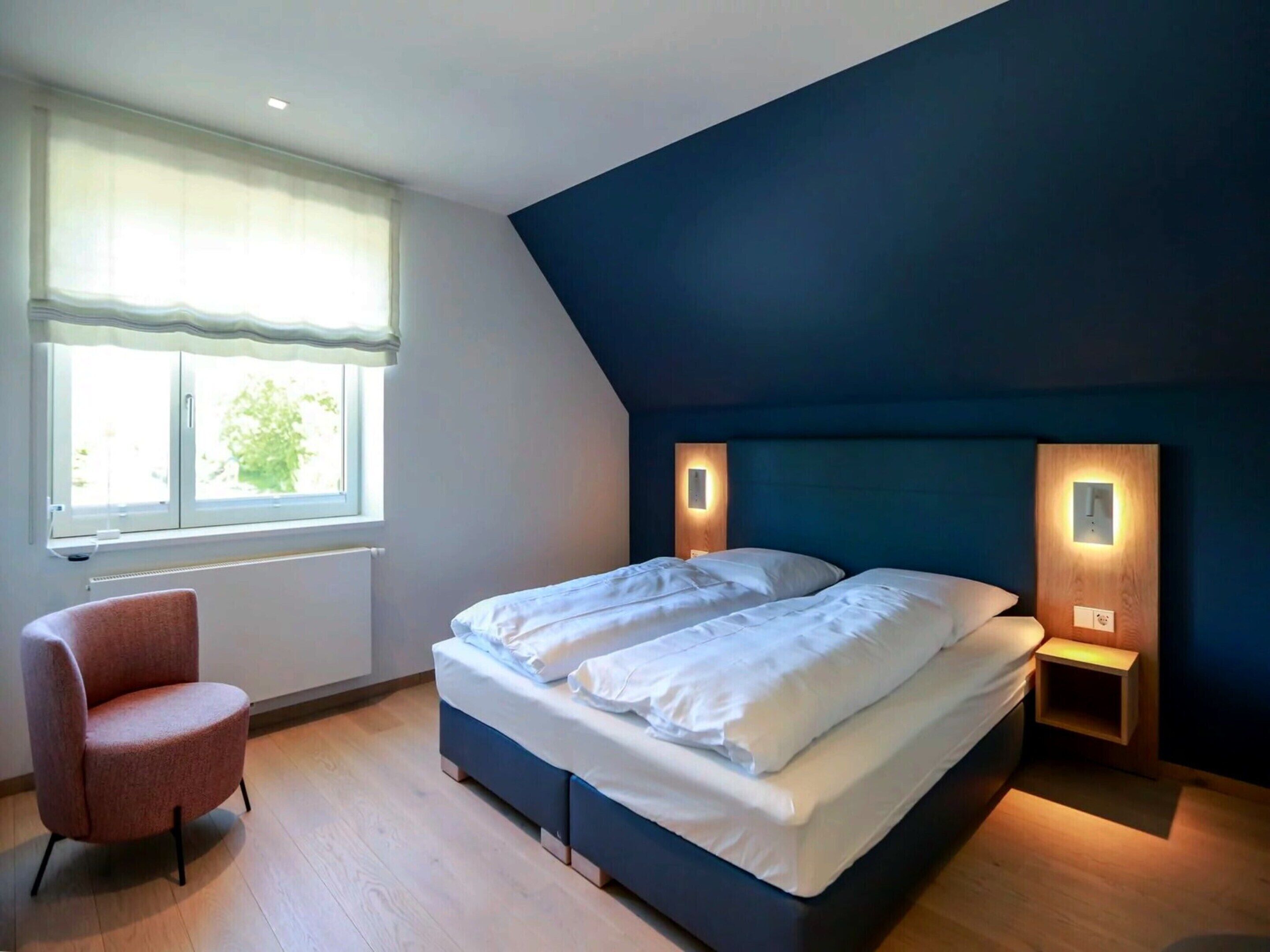 A bedroom with a bed, a chair, and a window.
