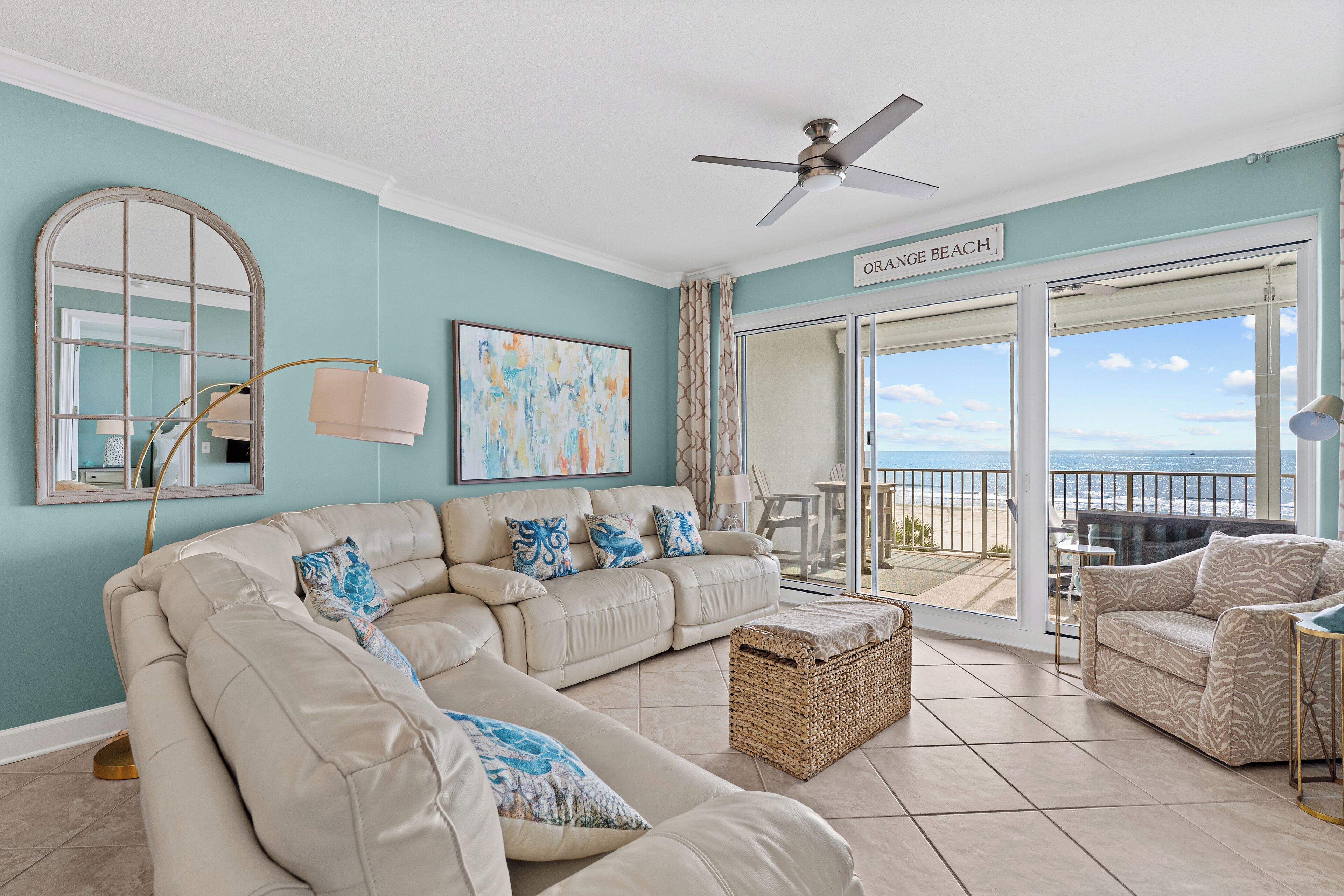 A living room with a large sectional sofa, a ceiling fan, and a view of the ocean through a sliding glass door.