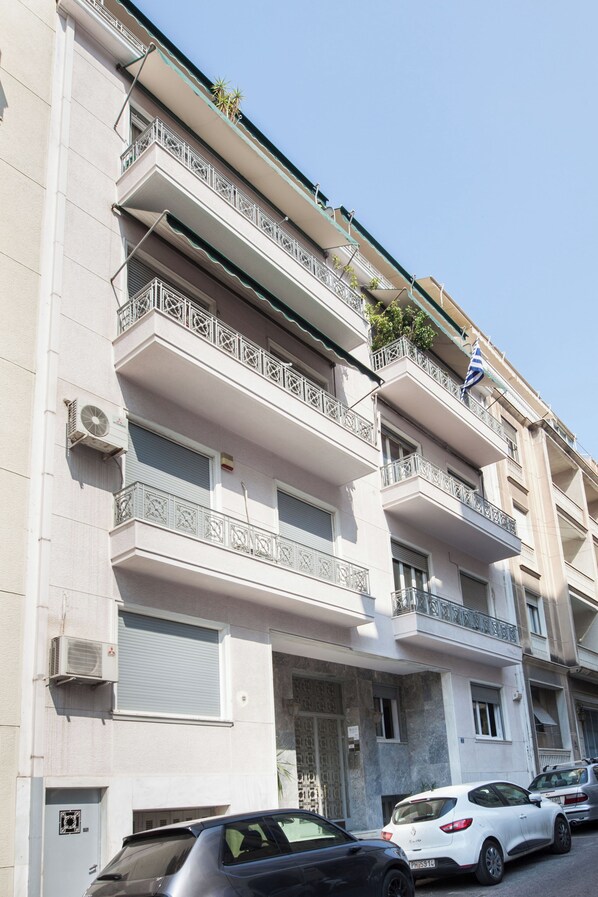 Un edificio de varios pisos con balcones, unidades de aire acondicionado y coches aparcados.