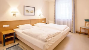 Ein Hotelzimmer mit zwei Betten, einem Nachttisch, einem Sessel und einem Fenster mit Vorhängen.