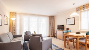 Ein modernes Wohnzimmer mit einer Couch, Sesseln, einem Esstisch mit Stühlen, einem Fernseher und einer Küchenzeile.