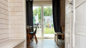 A room with wooden walls, a sliding glass door leading to a balcony, a dining table with chairs, and a small table with a chair. - Terraced Houses, Dziwnow (Dziwnów)