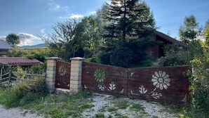 Ein hölzernes Tor mit floralen Verzierungen, ein großer immergrüner Baum und ein Haus mit rotem Dach im Hintergrund.