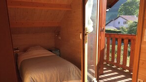 Ein Schlafzimmer einer Holzhütte mit einem Bett, einem kleinen Nachttisch und Blick auf eine Holzterrasse und die umliegende Natur.