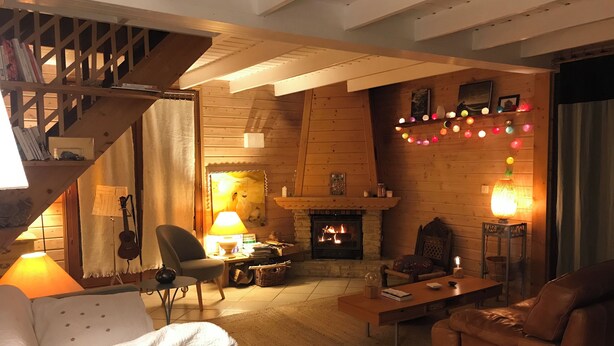 Ein gemütliches Wohnzimmer mit Kamin, Holzwänden, einer Treppe und einer Lichterkette mit bunten Lichtern.