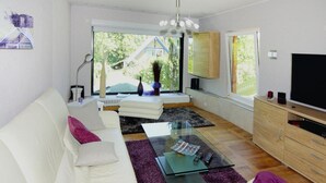 Ett modernt vardagsrum med en vit soffa, lila kuddar, ett glasbord och en tv som står på ett träskåp.