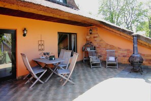 An outdoor patio with a table and chairs, a brick chimney, and a thatched roof. - Ferienhaus, Damerow (Jabel)