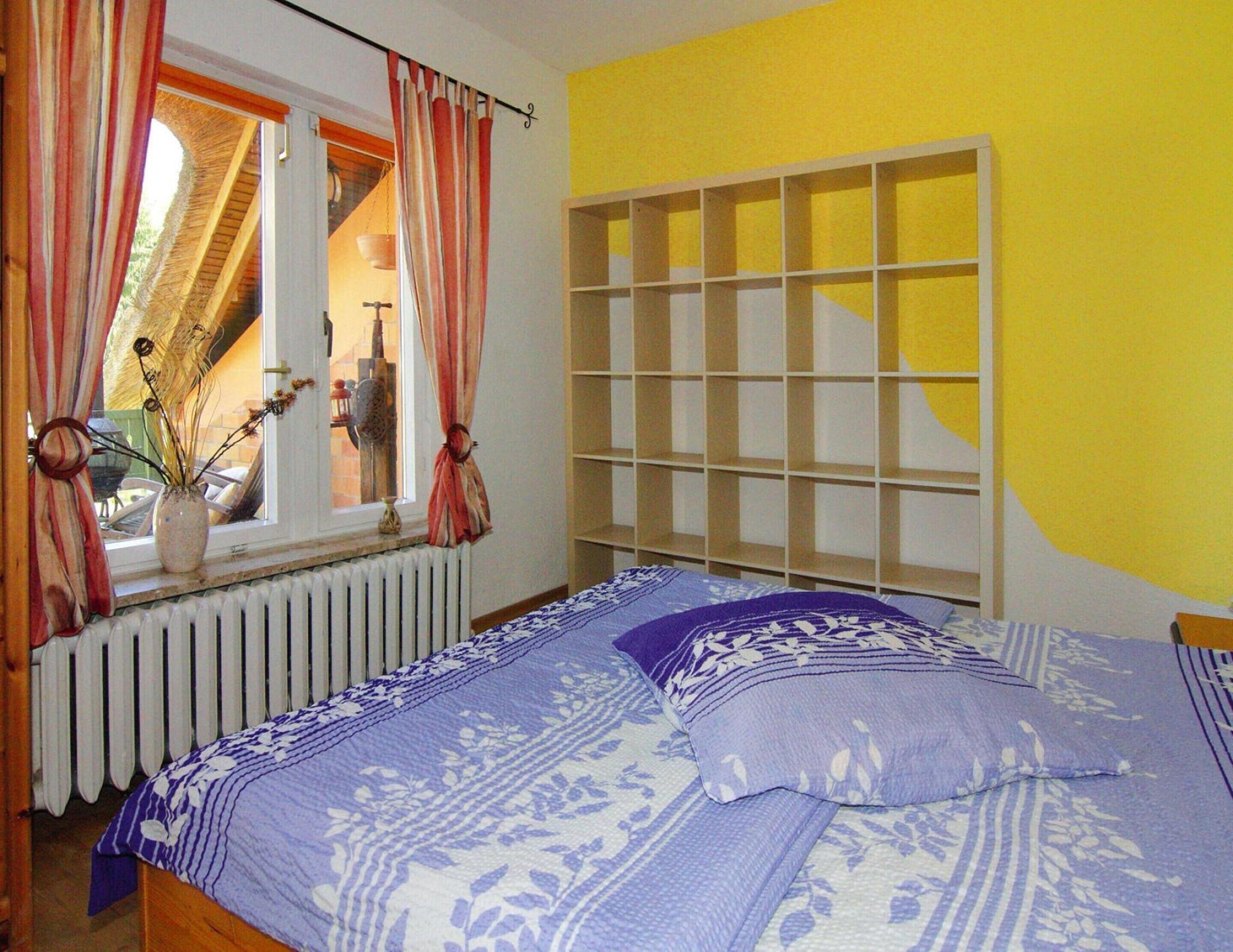 Une chambre à coucher avec un lit, une fenêtre avec des rideaux, un radiateur et une étagère.