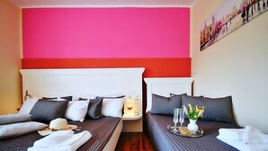 Hotellihuone, jossa on kaksi sänkyä, punainen tehosteseinä ja kaupunkimaisemaa esittävä taulu.