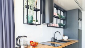 Μια σύγχρονη κουζίνα με έναν ξύλινο πάγκο, ένα βραστήρα, ένα μπολ με φρούτα και έναν μαύρο απορροφητήρα.