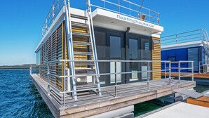 Ein schwimmendes Haus mit einer Holzterrasse, Metallgeländern und blauem Himmel im Hintergrund.