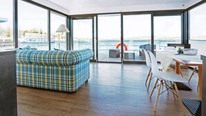 Ein modernes Wohnzimmer mit einer großen Couch, einem Esstisch mit Stühlen und Meerblick durch große Fenster.