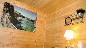 Une chambre dans une cabane en bois, avec un lit, un tableau représentant un paysage côtier, une lampe de chevet et une petite statue blanche.