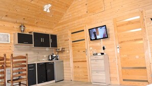 Un intérieur en bois comprenant un coin cuisine, un téléviseur fixé au mur et un petit meuble.