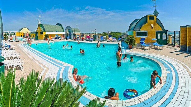 Una gran piscina al aire libre rodeada de sillas de descanso y zonas de sol, con un cielo despejado.